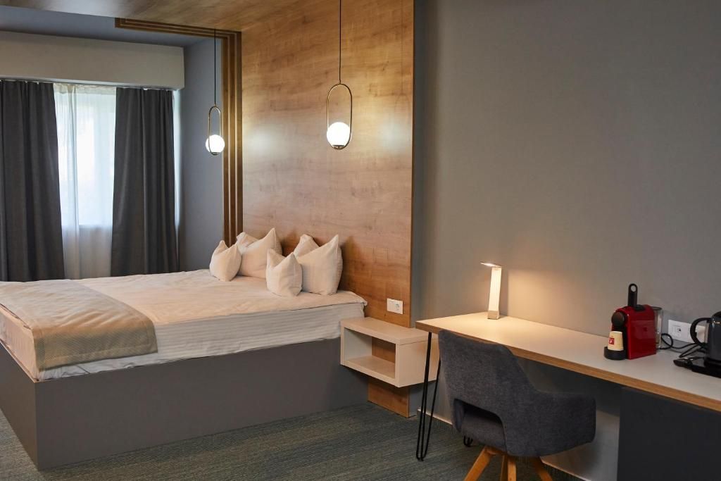 A hotel room with a bed, bedside table, desk, chair, and a wall-mounted light fixture.