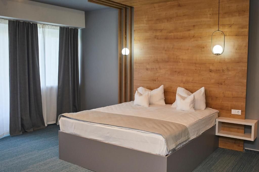 A hotel room with a large bed, a wooden headboard, a bedside table, and a window with curtains.