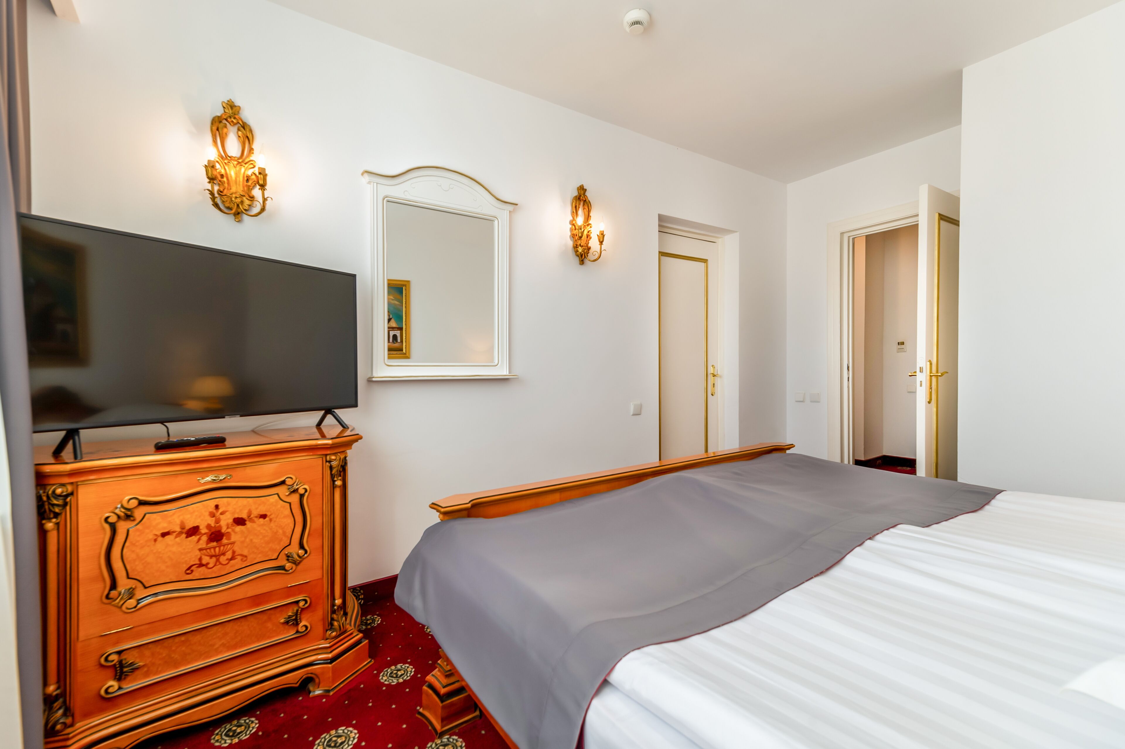 Une chambre d’hôtel comprenant un lit, une commode avec un téléviseur à écran plat, deux appliques murales et une porte.
