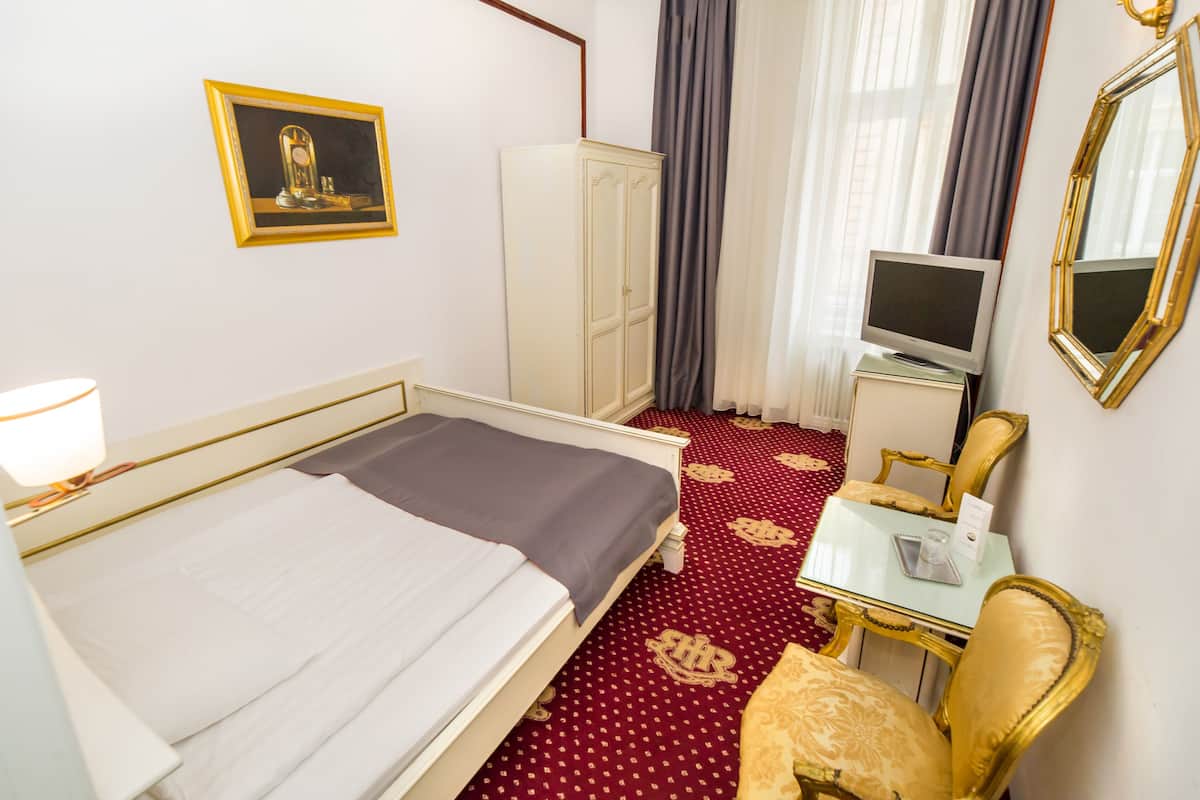 A hotel room with a bed, a desk with a television, a wardrobe, and a chair.