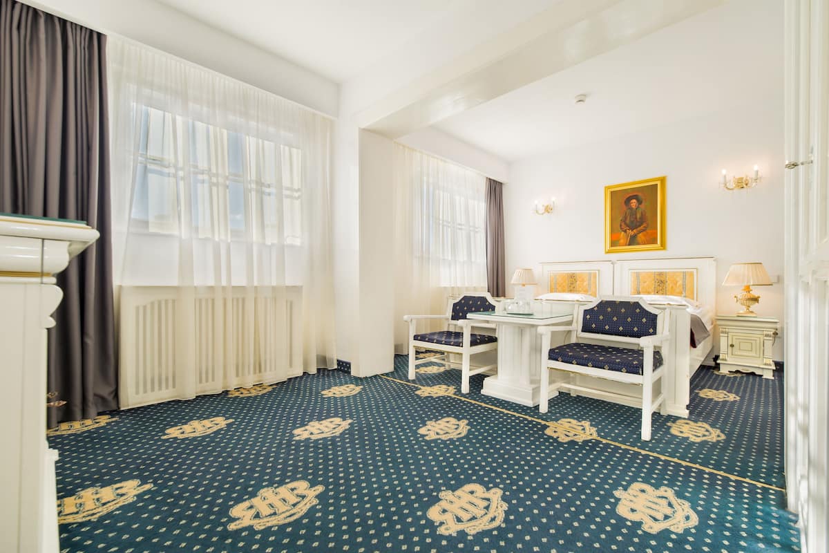 A hotel room with a patterned carpet, a bed, a table with chairs, and a painting on the wall.
