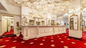 A grand hotel lobby with a red carpet, ornate chandeliers, and a large reception desk. - Hotel Imparatul Romanilor (Sibiu)