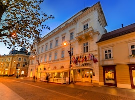 Un hotel histórico con arquitectura clásica, una calle empedrada y banderas en el balcón.