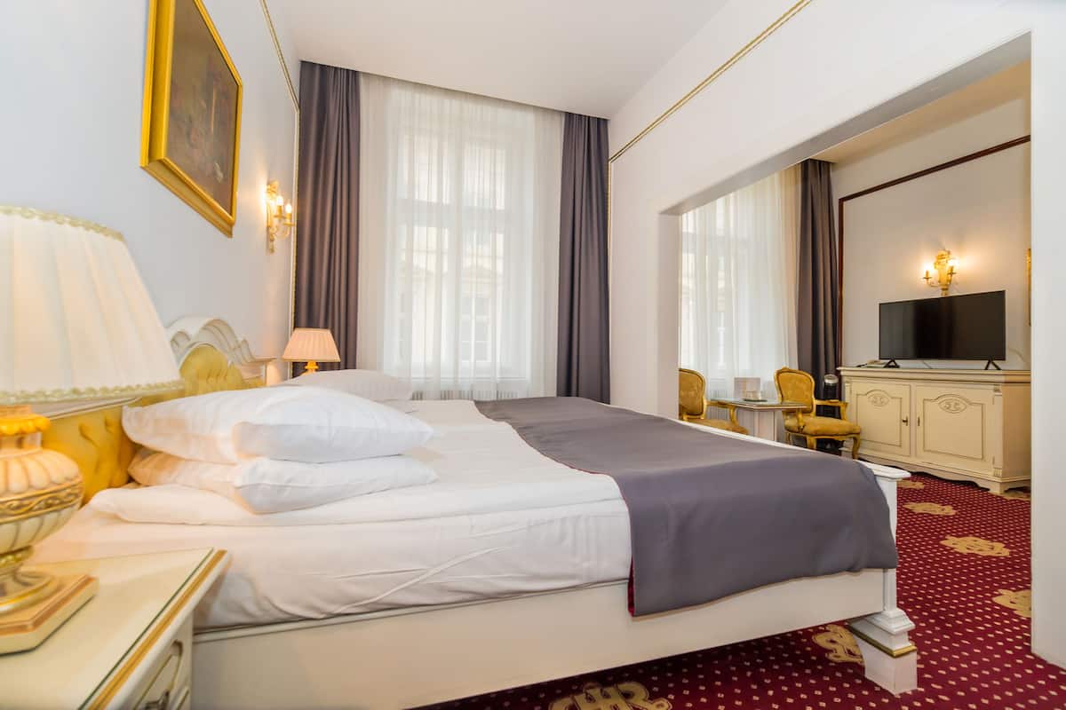 A hotel room with a large bed, a desk with a lamp, a television, and a wardrobe.
