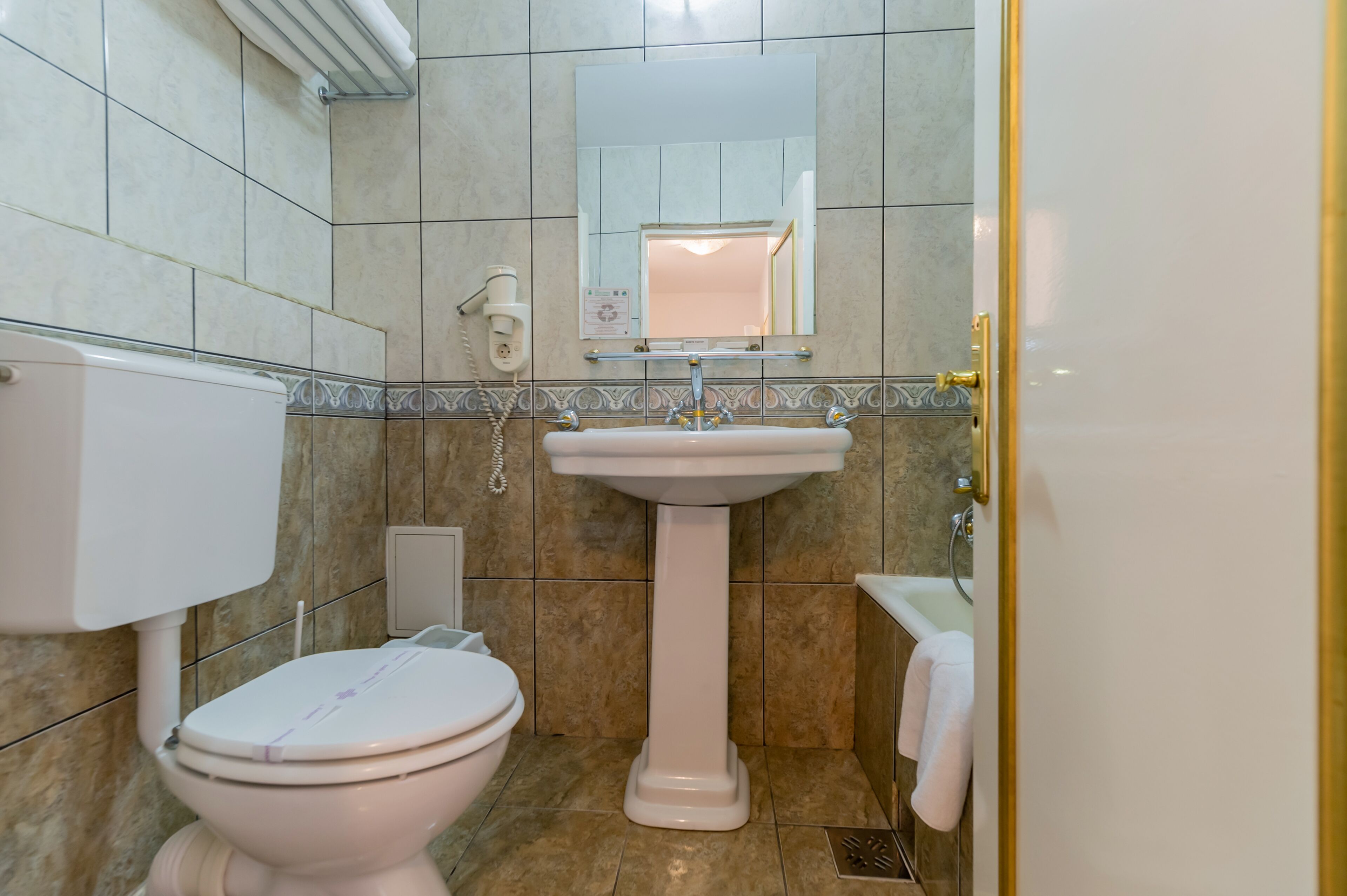 A bathroom with a toilet, pedestal sink, and a mirror above the sink.
