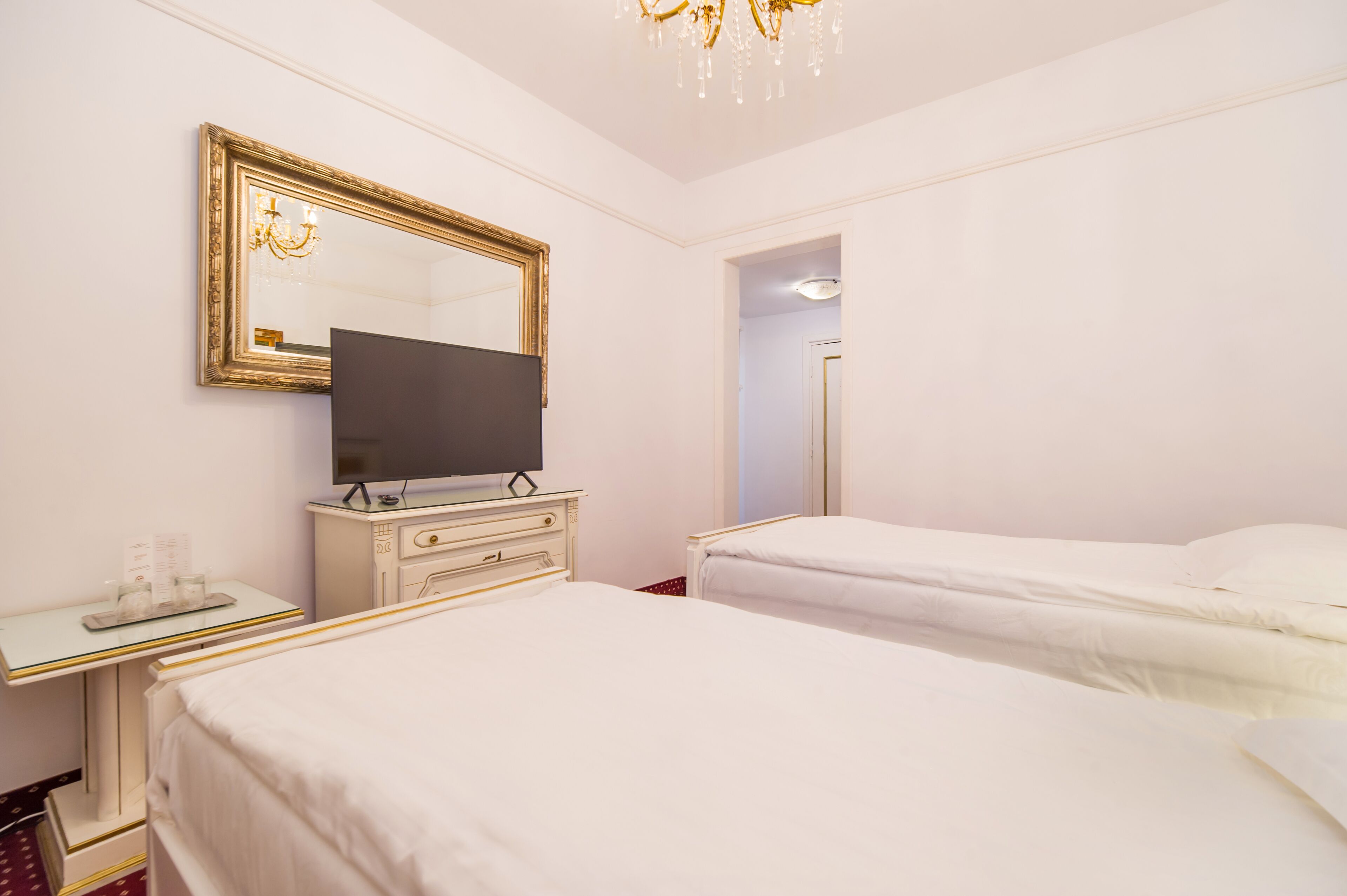 Una habitación de hotel con dos camas, un televisor en una cómoda, un espejo y una araña.