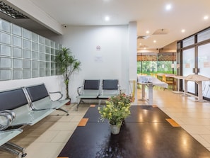 A waiting area with metal chairs, a potted plant, and a table with a white tablecloth.