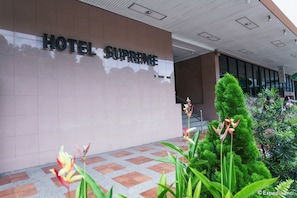 The exterior of Hotel Supreme with a tiled entrance and a well-maintained garden area.