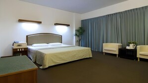 Ein Hotelzimmer mit einem Bett, zwei Nachttischlampen, einem Schreibtisch, einem Stuhl und einem großen Fenster mit Vorhängen.