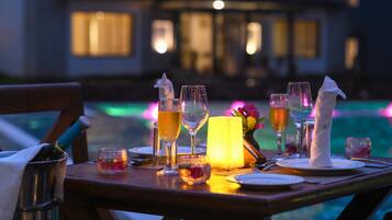 A dining table set with glasses, a candle, and a bottle, overlooking a pool.