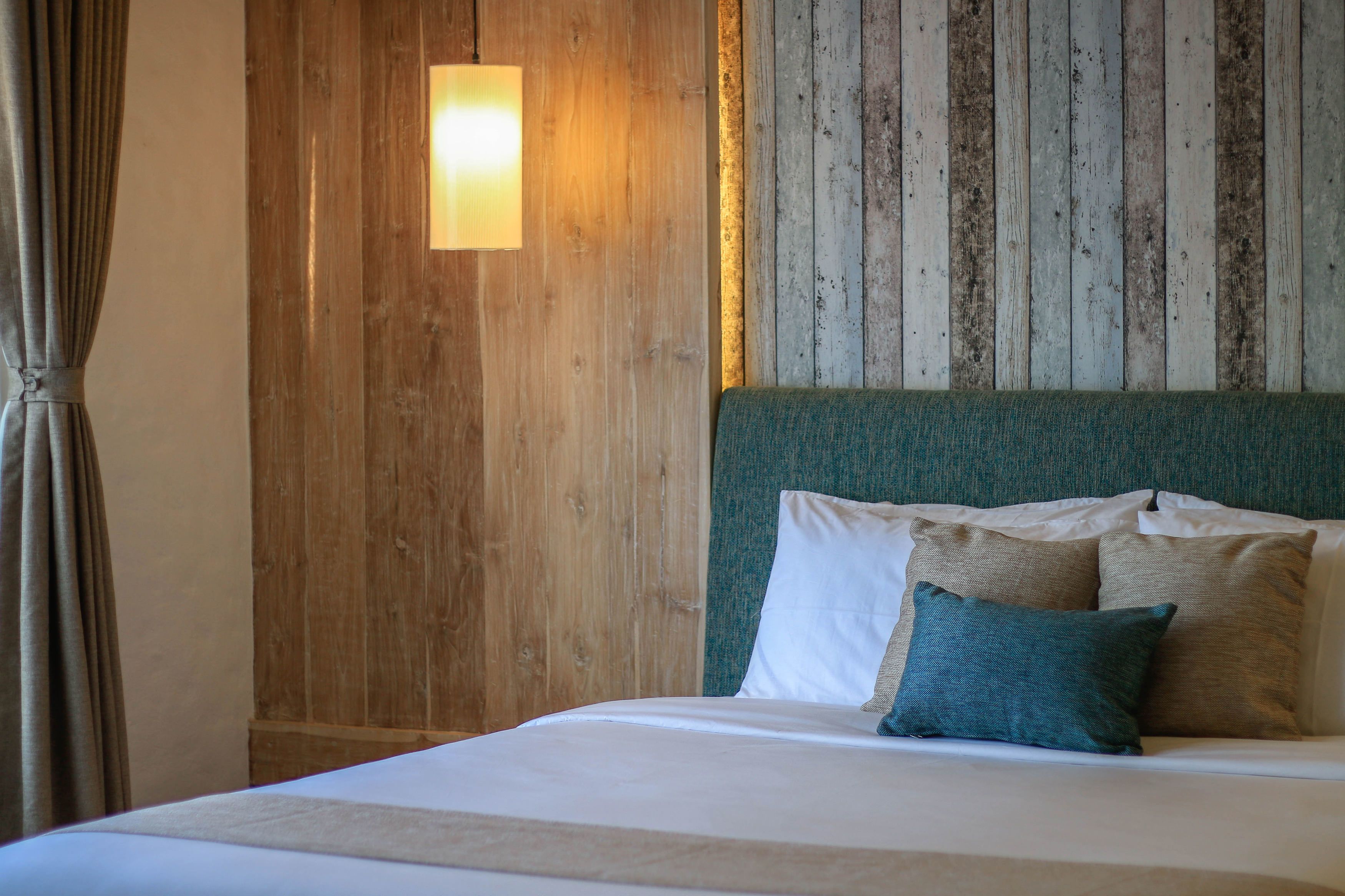 Una cama con ropa de cama blanca y dos almohadas, una pared de madera con un diseño de rayas verticales y una lámpara colgante.