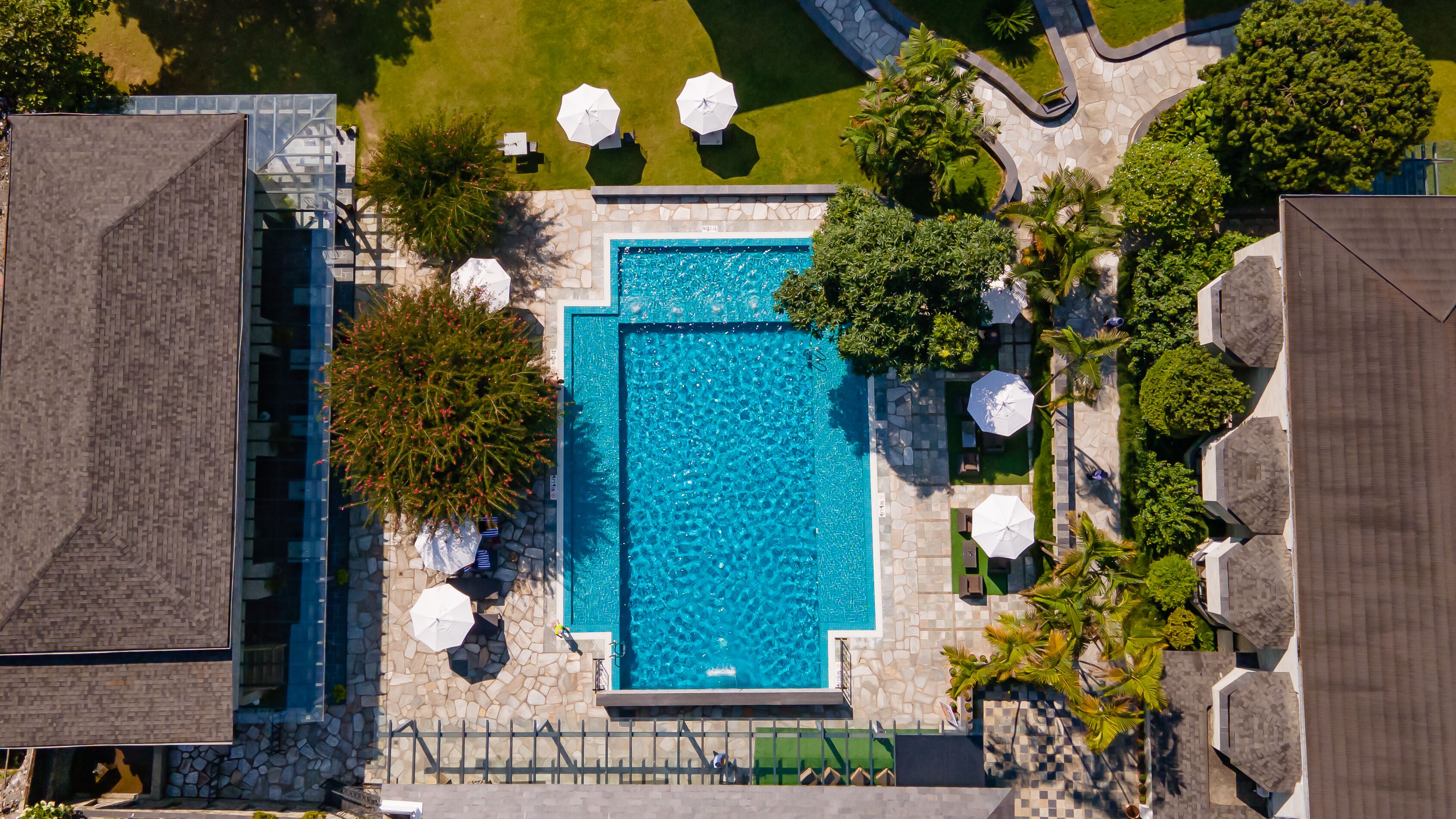 An aerial view of a swimming pool surrounded by stone walls and greenery, with umbrellas and outdoor seating.