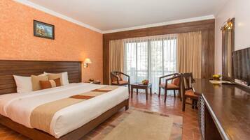 A hotel room with a large bed, two chairs, a desk, and a TV.