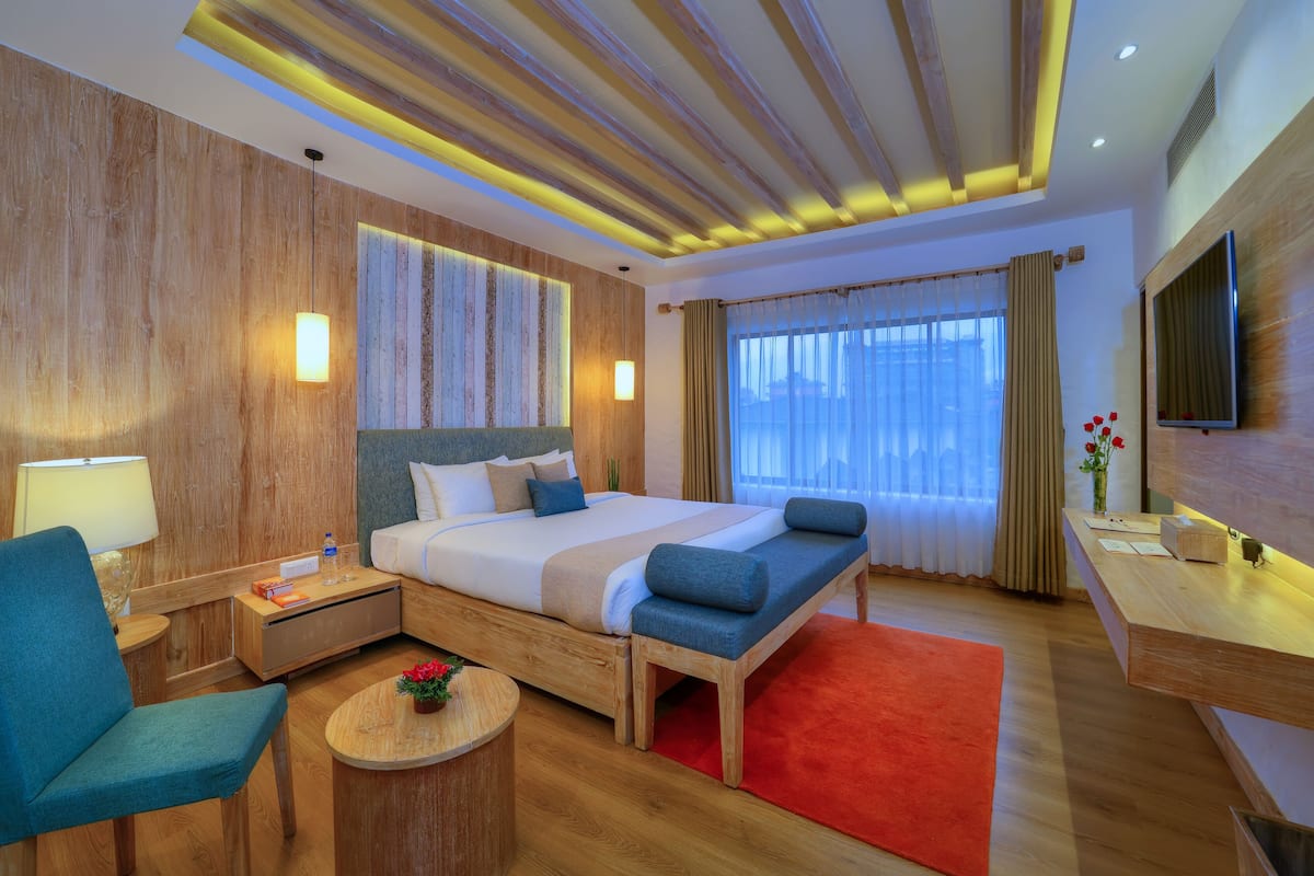 A modern hotel room with a large bed, a desk, a chair, a TV, and a window with curtains.