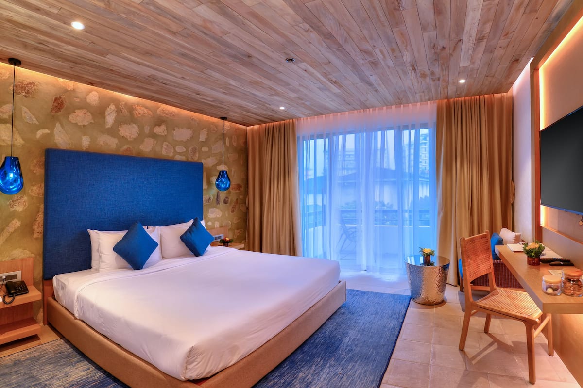A hotel room with a large bed, a desk with a chair, a TV, and a window with curtains.