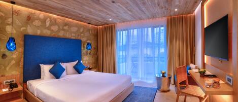 A hotel room with a large bed, a desk with a chair, a TV, and a window with curtains.