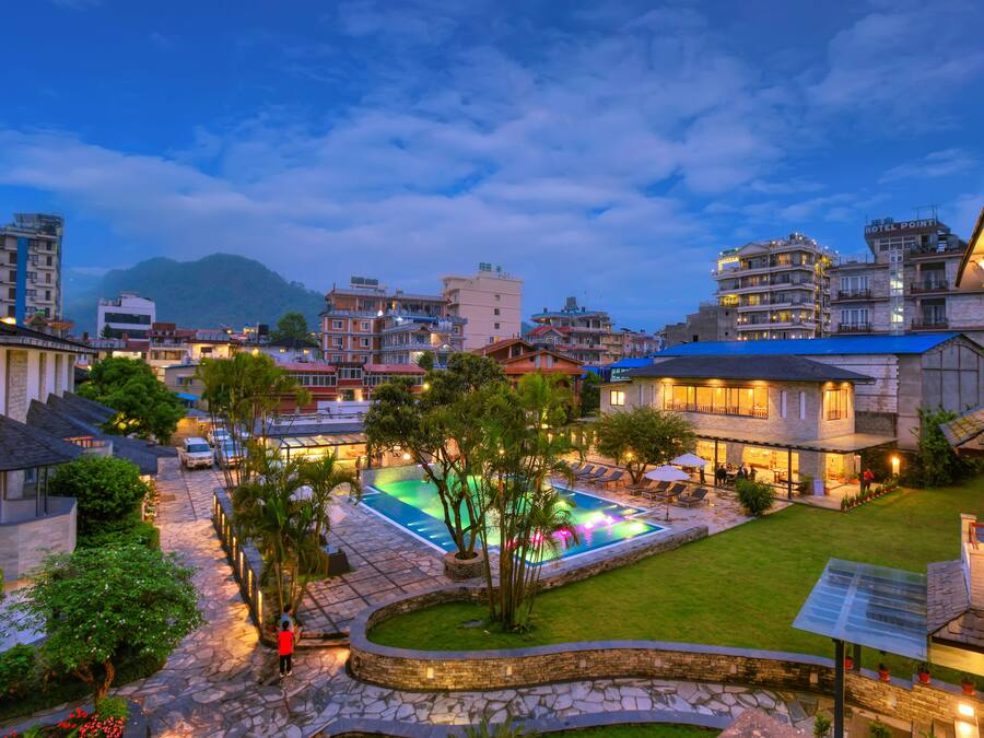 A hotel courtyard with a swimming pool, stone pathways, and surrounding greenery.