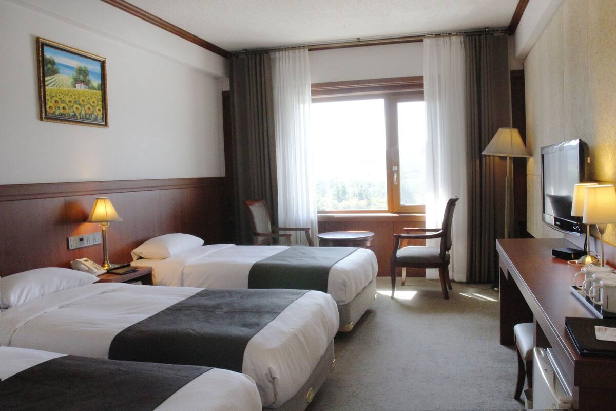 A hotel room with two beds, a desk with a television, a chair, and a window with curtains.