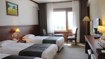 A hotel room with two beds, a desk with a television, a chair, and a window with curtains.
