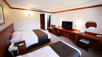 A hotel room with two beds, a desk with a television, and a small seating area.