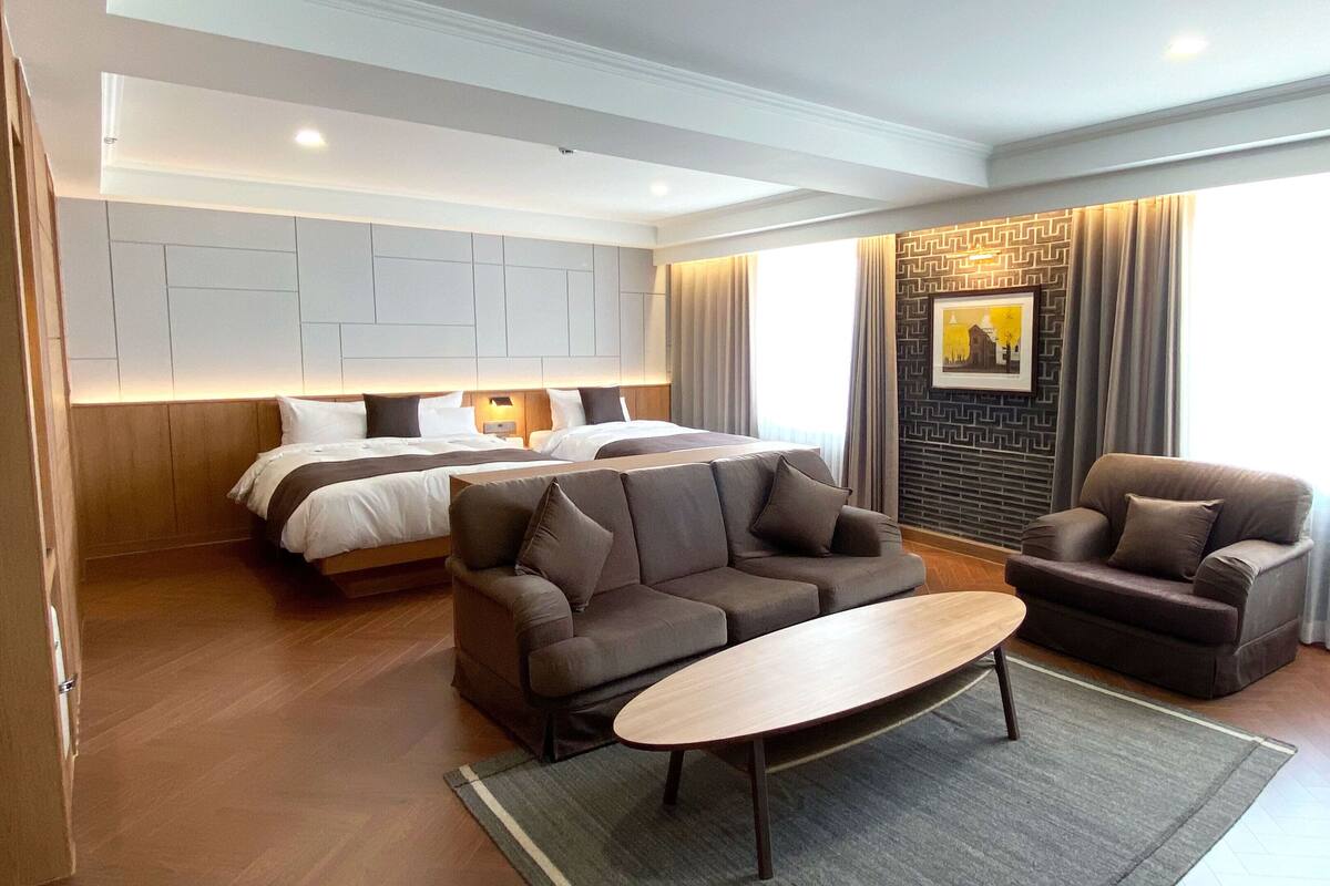 A hotel room with a large bed, two sofas, a coffee table, and a view of the city through the window.