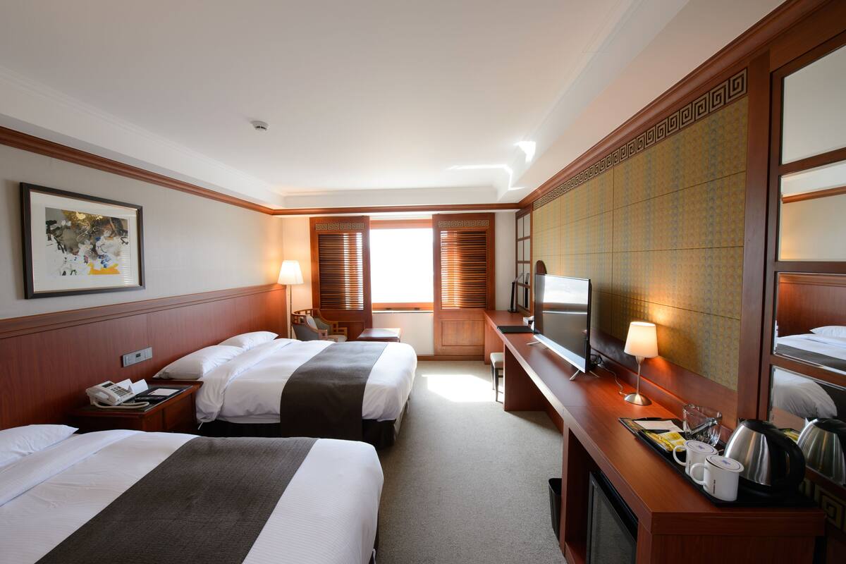 A hotel room with two beds, a desk with a TV, a telephone, and a coffee maker.