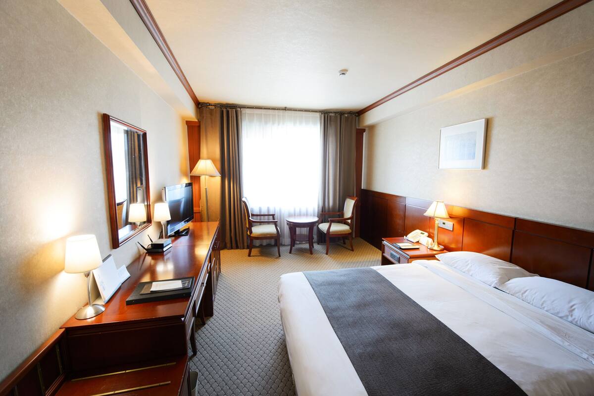 A hotel room with a bed, desk, chairs, and a TV.