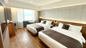A hotel room with two beds, a desk, a chair, a small table, and a window with curtains. - Commodore Hotel Gyeongju (Gyeongju)