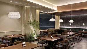 A restaurant with wooden tables and chairs, pendant lights, and a large window with a view. - Commodore Hotel Gyeongju (Gyeongju)