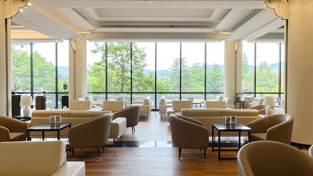 A spacious lounge area with multiple seating options, large windows offering a view of greenery and hills, and a modern ceiling design. - Commodore Hotel Gyeongju (Gyeongju)