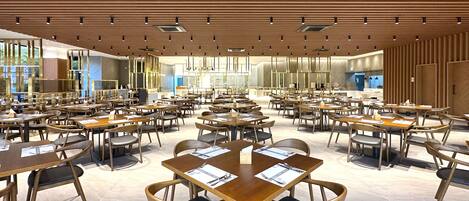 Een ruim restaurant met meerdere tafels en stoelen, een houten plafond en grote ramen die veel natuurlijk licht binnenlaten.