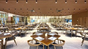 A spacious restaurant with multiple tables and chairs, a wooden ceiling, and large windows allowing natural light.
