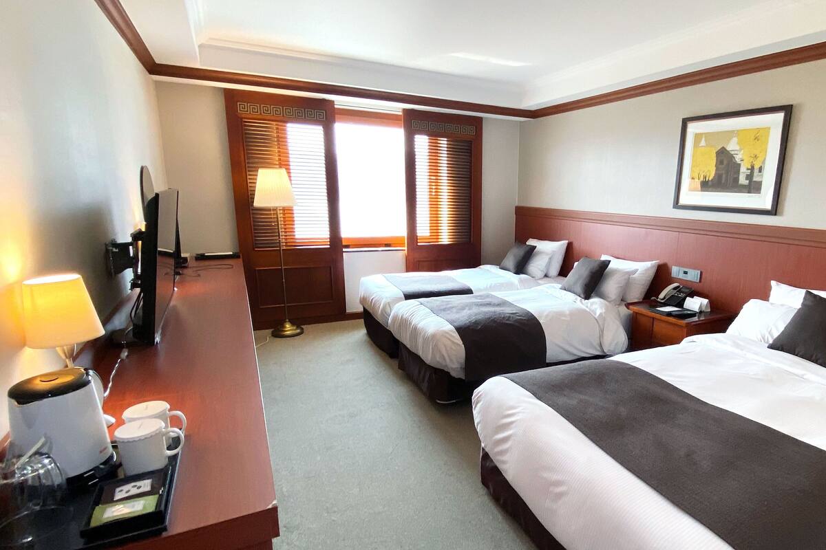 A hotel room with two beds, a desk with a lamp, a telephone, and a picture on the wall.