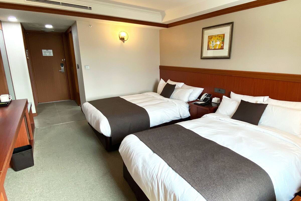 A hotel room with two beds, a desk, a phone, and a framed picture on the wall.