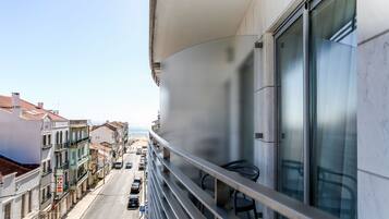 Een balkon met uitzicht op een straat en gebouwen, een hekwerk en een glazen deur.