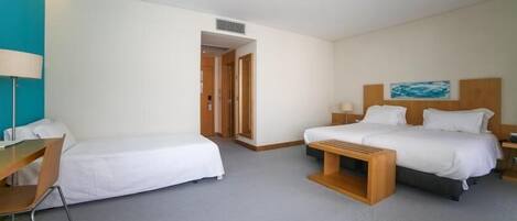 A hotel room with two beds, a desk, and a chair. There is a painting on the wall and a door leading to another room.