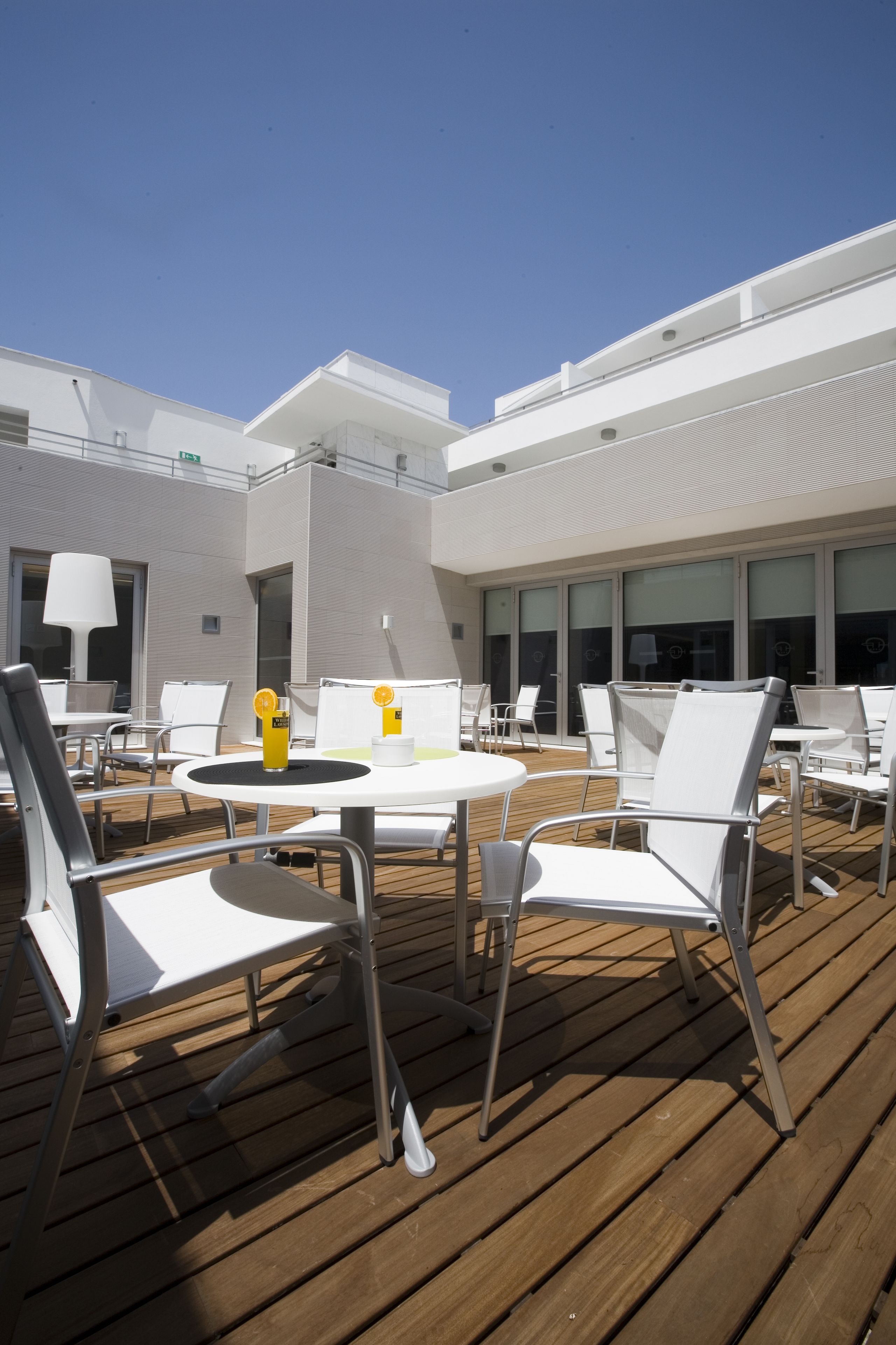 A deck with white chairs and tables, a yellow drink, and a modern building in the background.