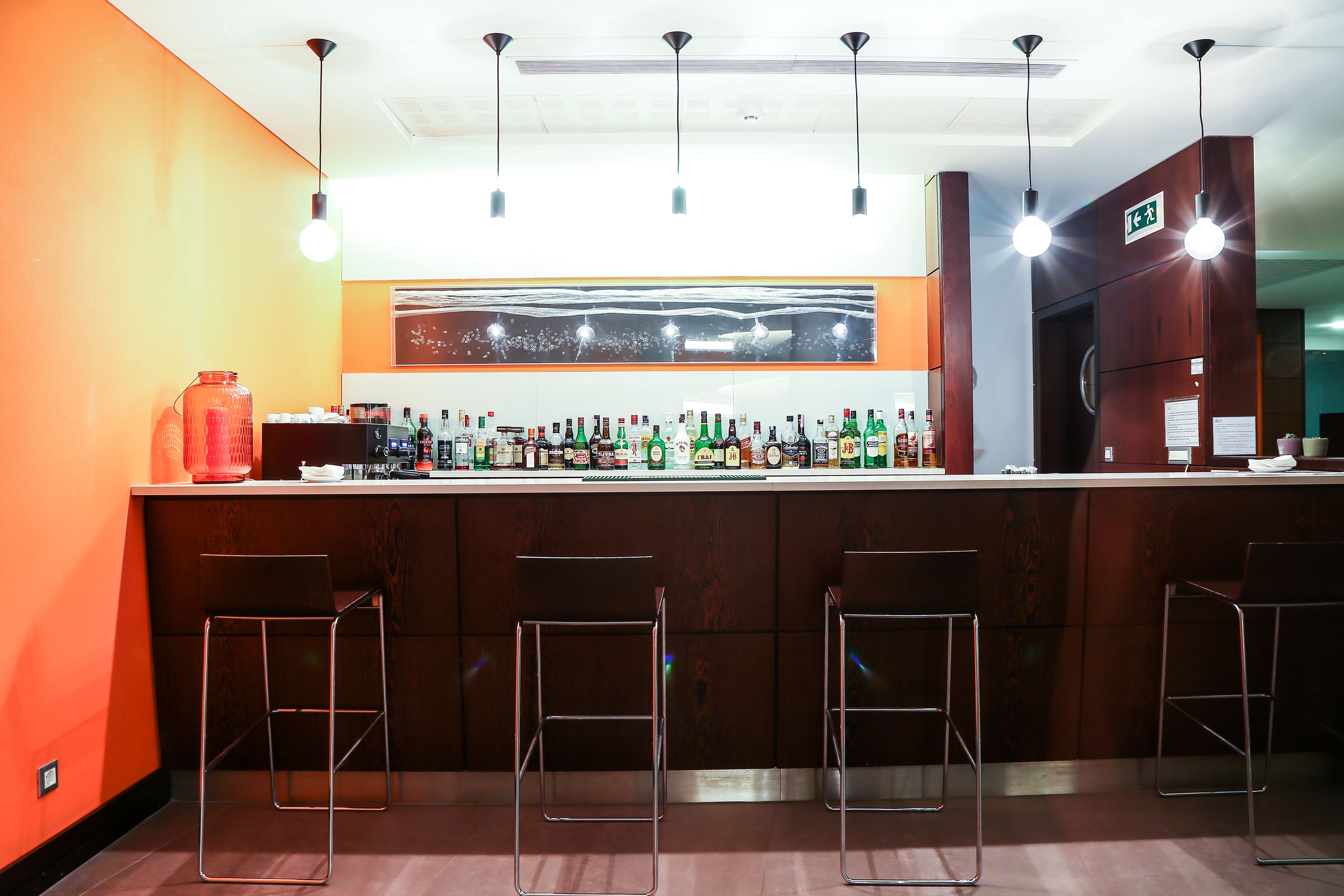 Een bar met een houten toonbank, diverse flessen en drie metalen barkrukken.