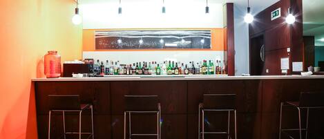 Een bar met een houten toonbank, diverse flessen en drie metalen barkrukken.