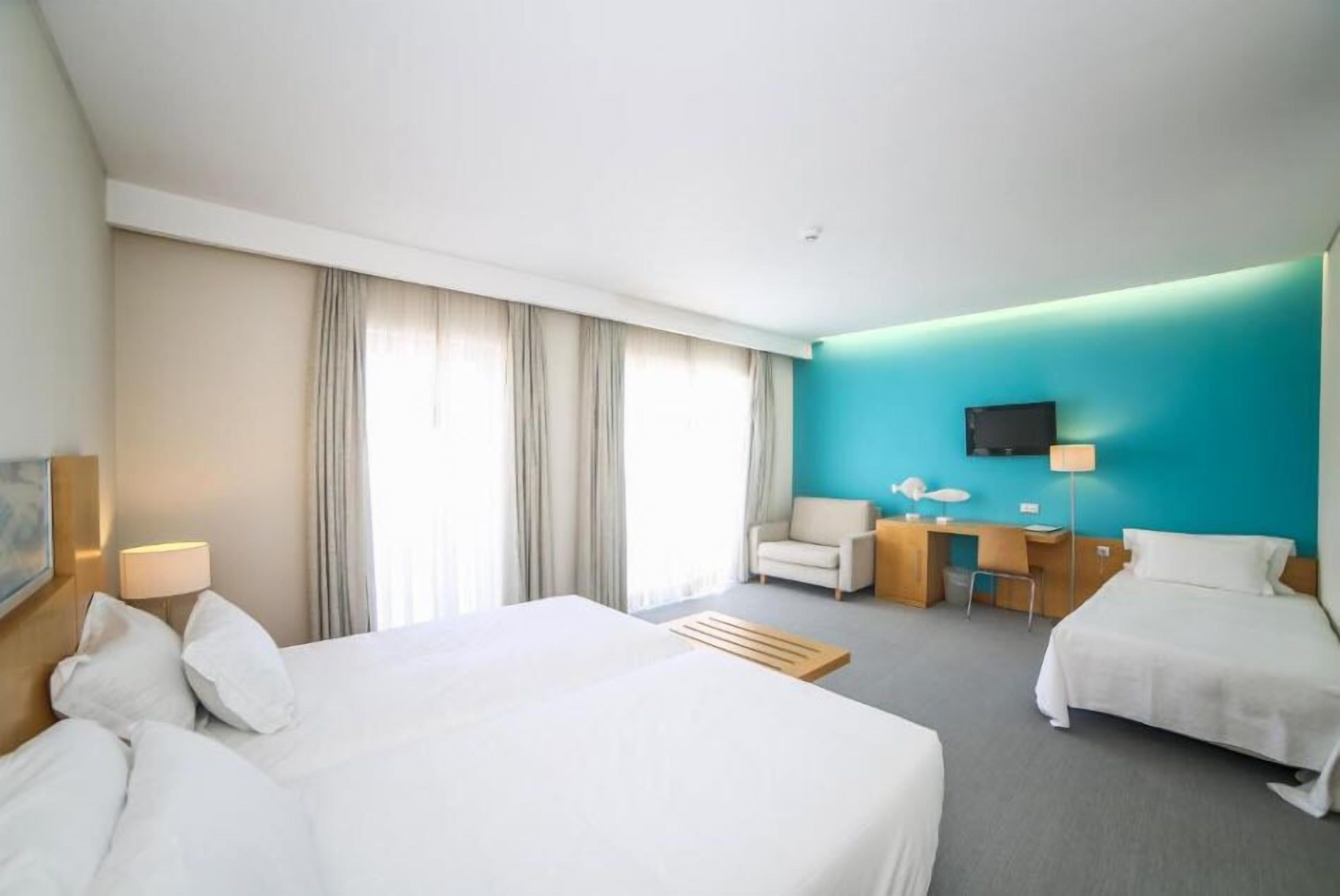 Habitación de hotel con dos camas, un escritorio, una silla, un televisor y una ventana con cortinas.