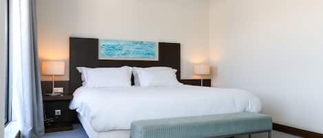 A hotel room with a large bed, two bedside lamps, a bench, and a painting on the headboard.