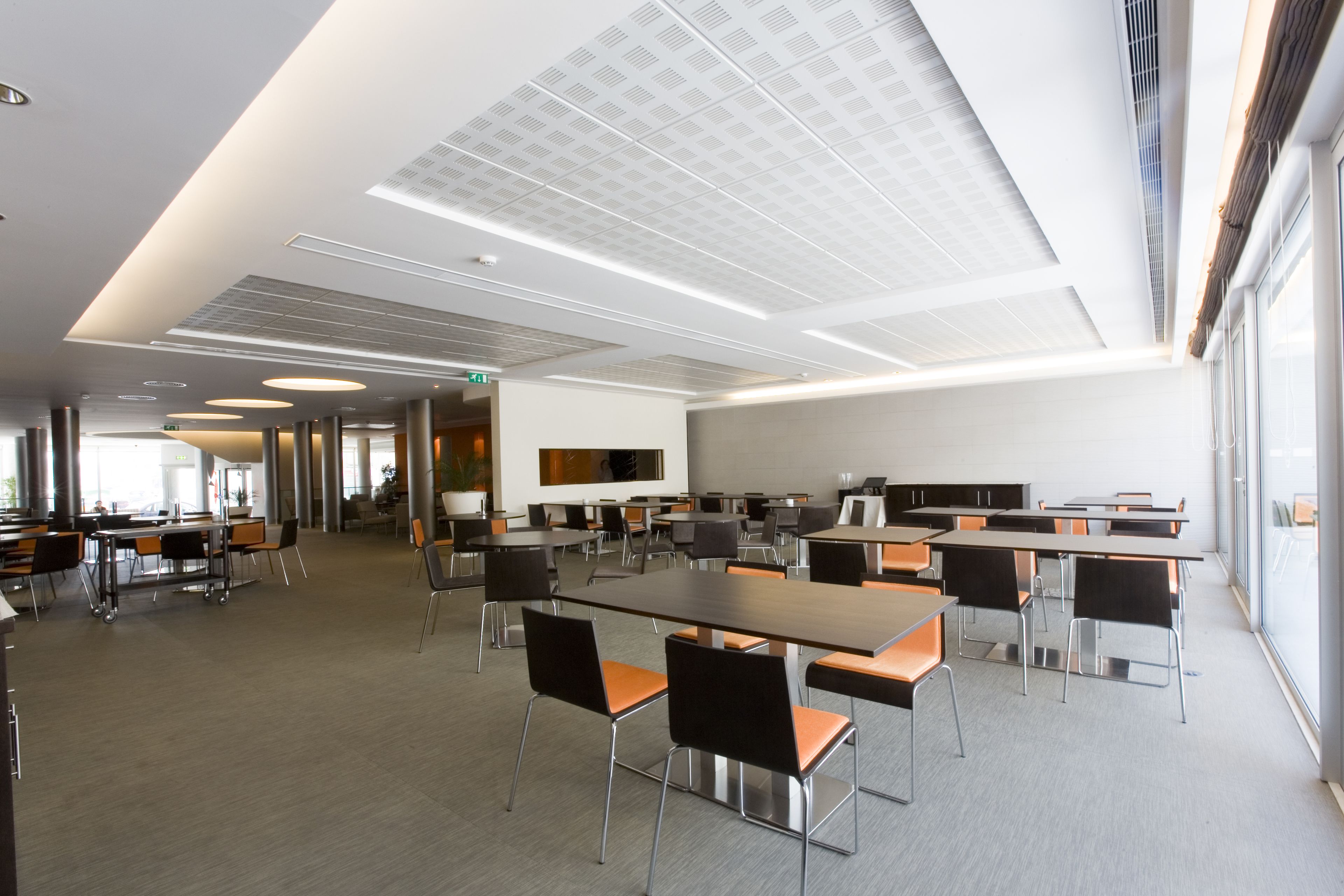 Una sala de conferencias moderna con varias mesas y sillas, ventanas amplias y un diseño limpio y minimalista.
