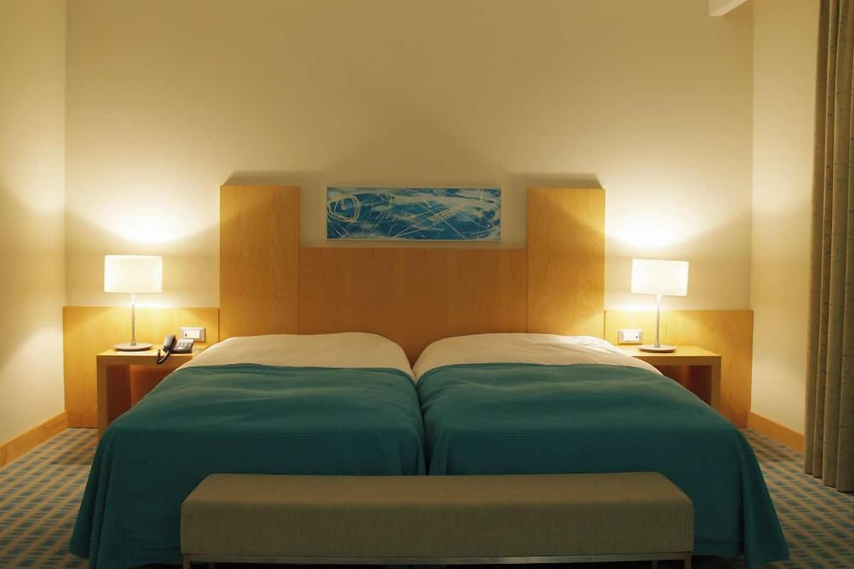 Ein Doppelbett mit Kopfteil, zwei Nachttischlampen, ein Telefon und ein Gemälde über dem Bett.