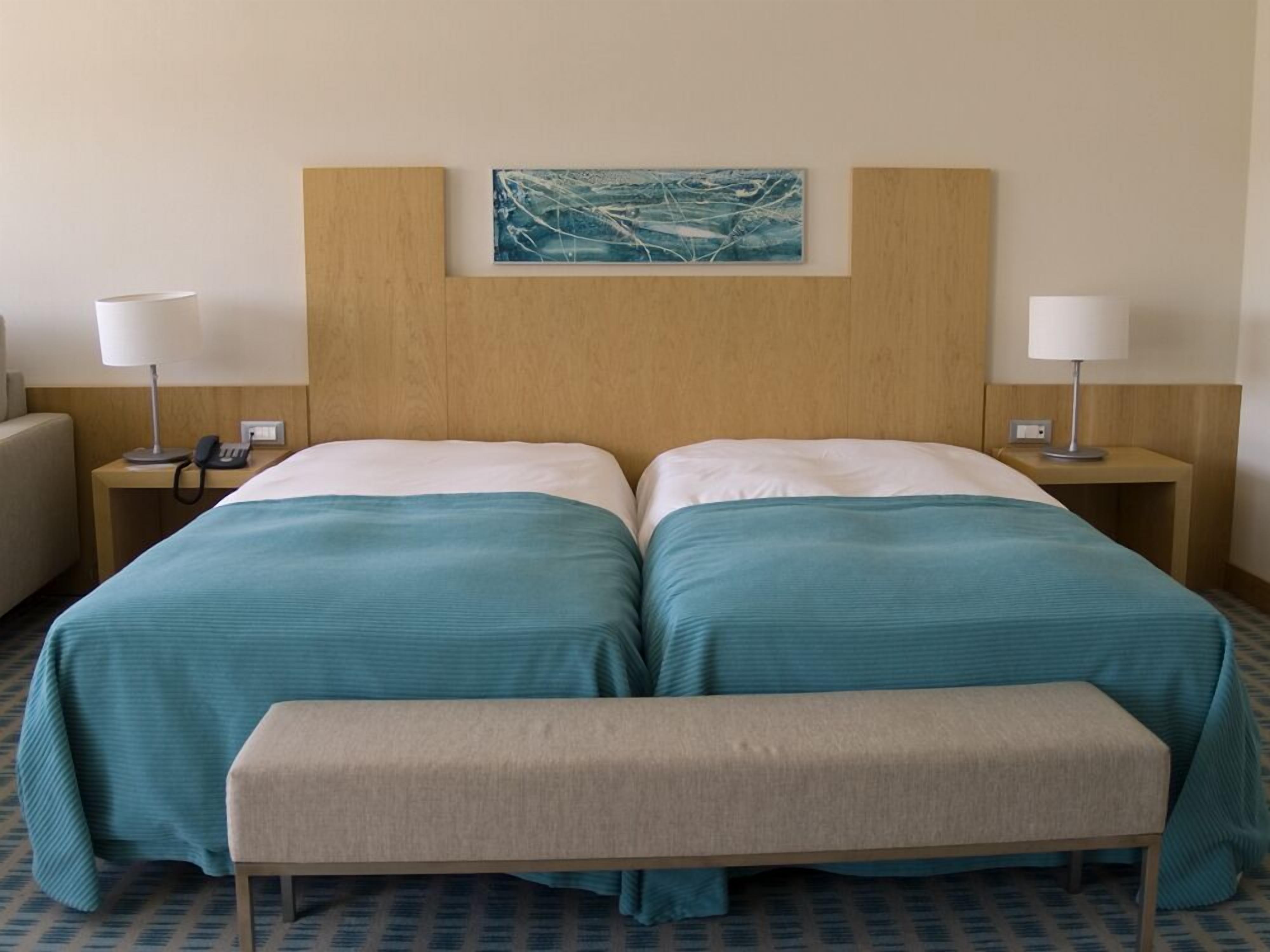A hotel room with two beds, a bench, and a painting on the wall.