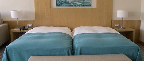 A hotel room with two beds, a bench, and a painting on the wall.