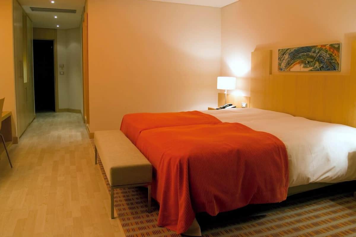 Ein Hotelzimmer mit einem Bett, einer Bank, einem Nachttisch mit Lampe und einem Bild an der Wand.