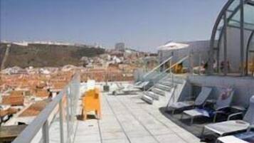 Une terrasse sur le toit offrant une vue dégagée sur le paysage urbain, avec une balustrade en verre et plusieurs fauteuils confortables.
