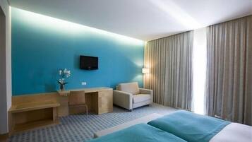 A hotel room with a bed, a desk, a chair, a television, and a window with curtains.
