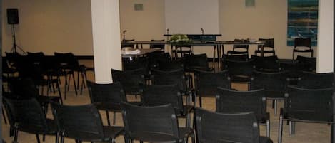 Un salón de conferencias con filas de sillas negras, una pizarra y una pantalla de proyector.