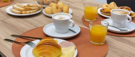 Una mesa de desayuno con cruasanes, queso, café y jugo de naranja.